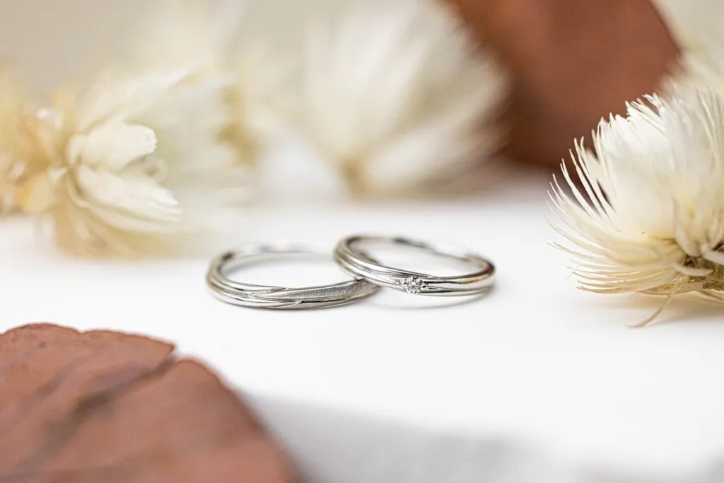 Silver wedding rings beside decorative flowers.