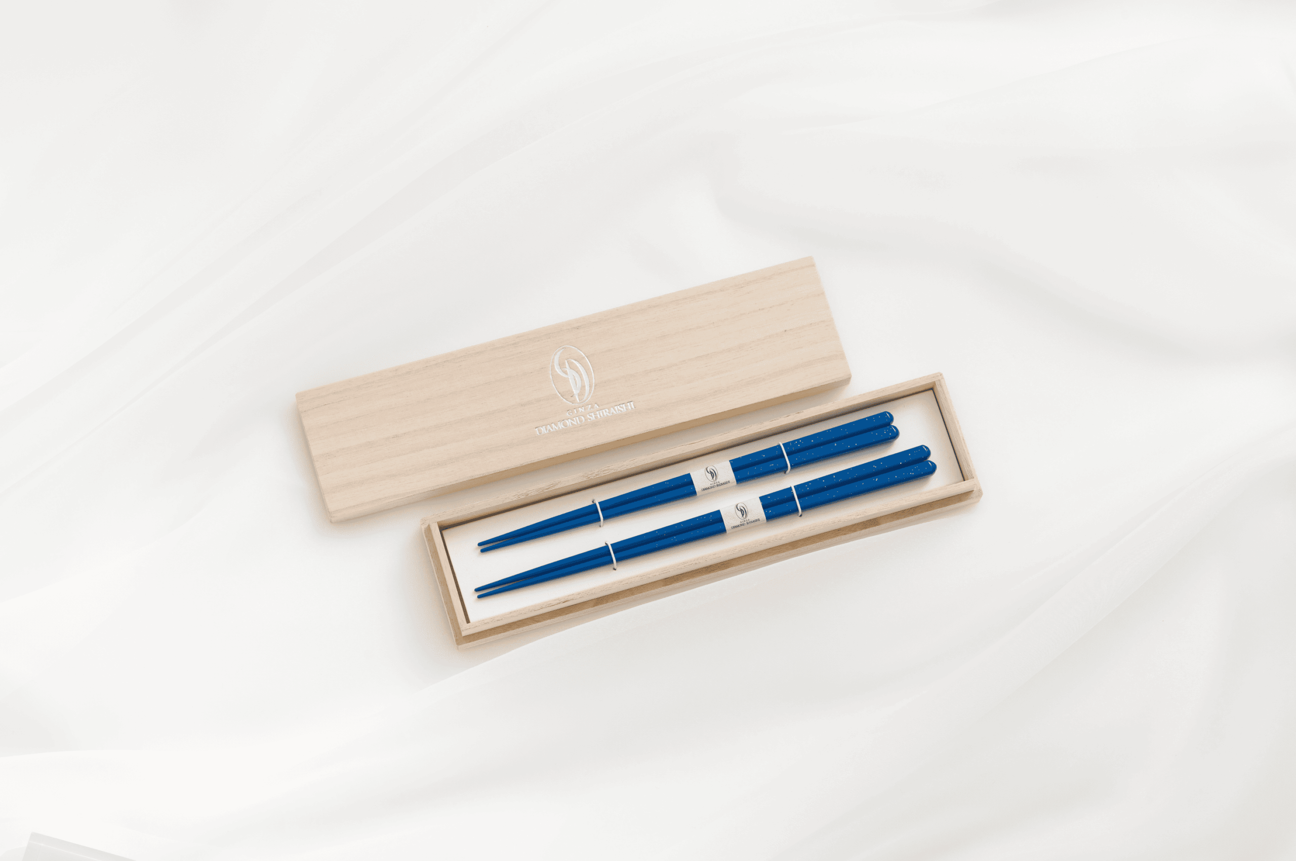 Blue chopsticks in a wooden box on white fabric.